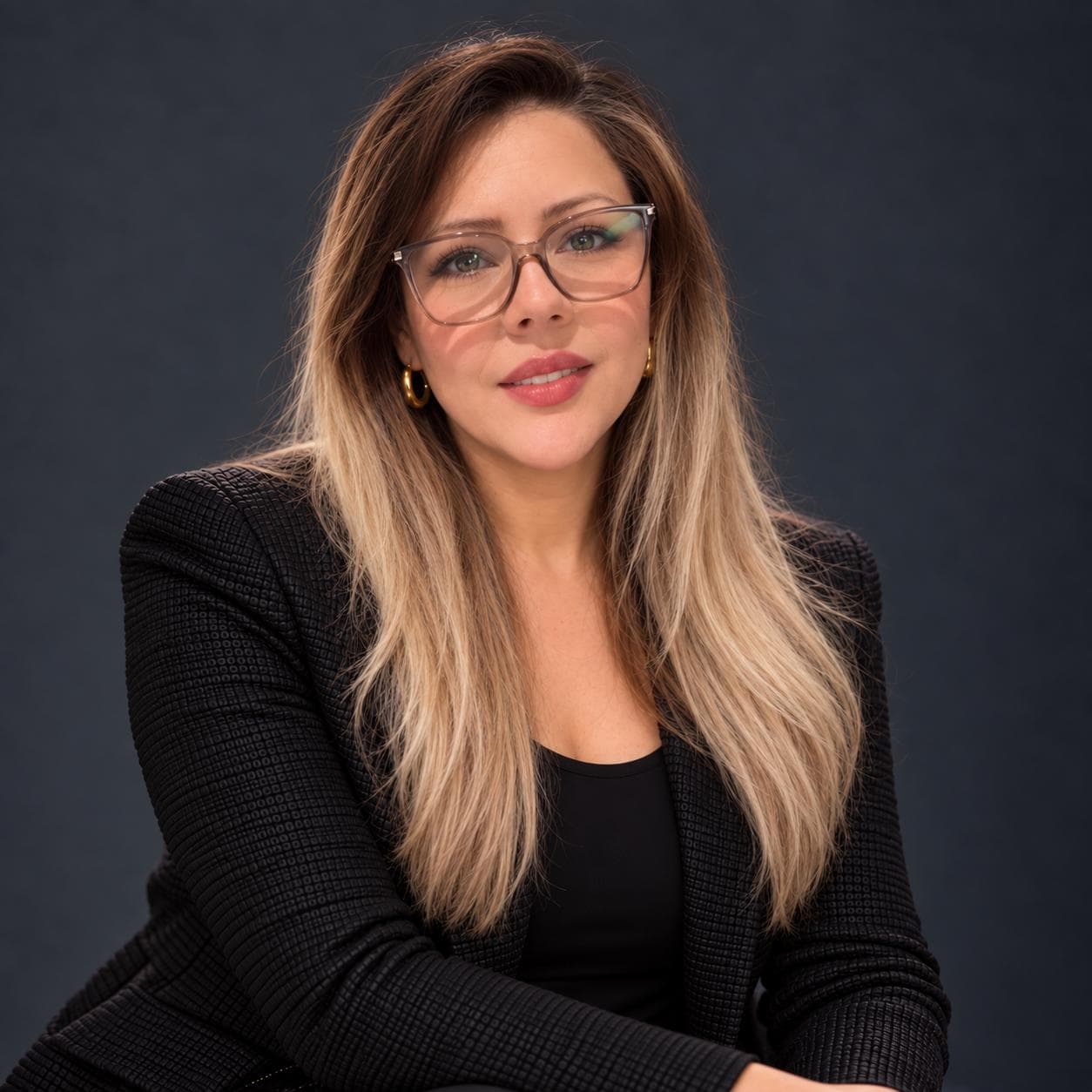 Professional woman with glasses and long blonde hair wearing a black textured blazer.